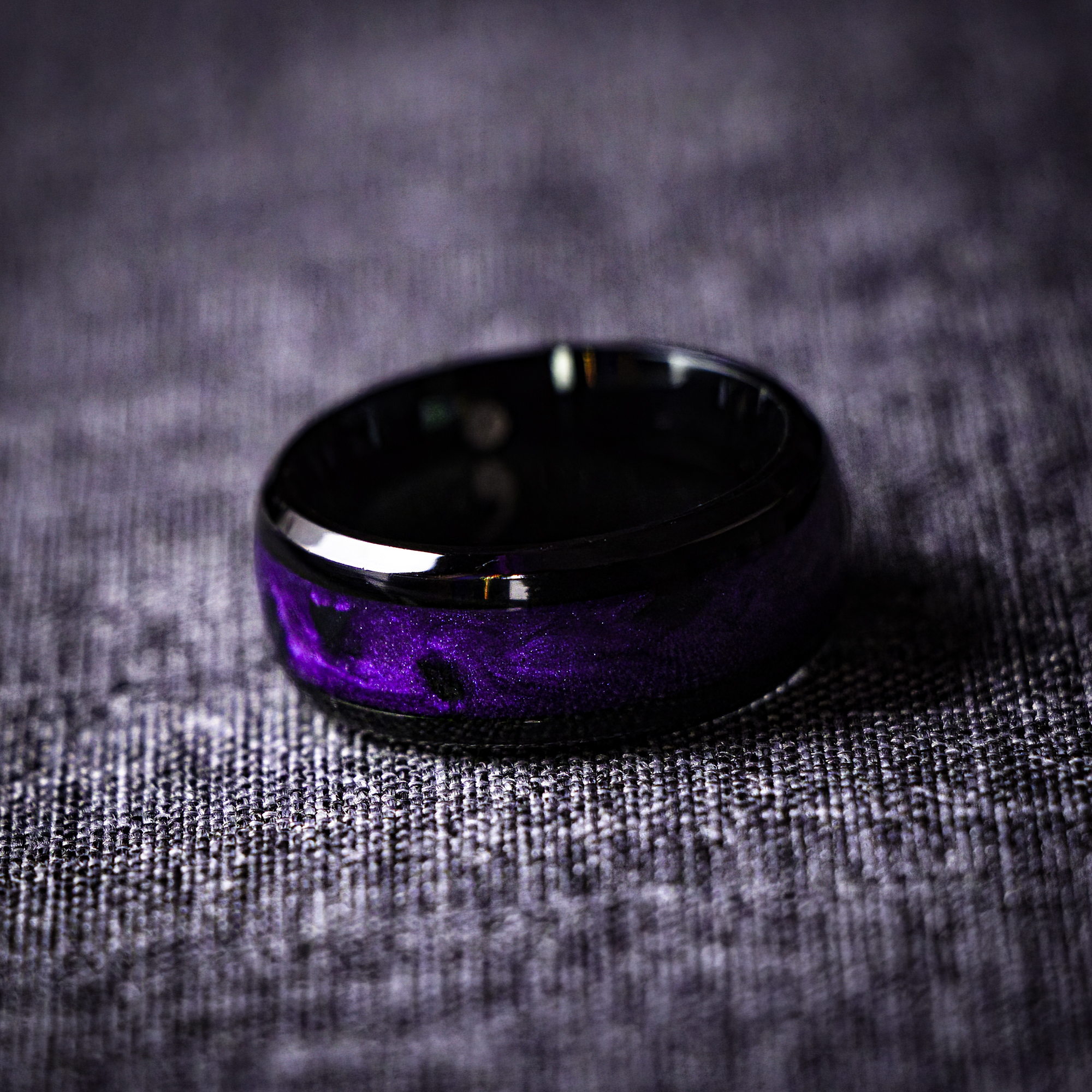 A black ring with iridescent violet pigments and pieces of black onyx stone inlaid around the band, creating a textured and organic pattern.